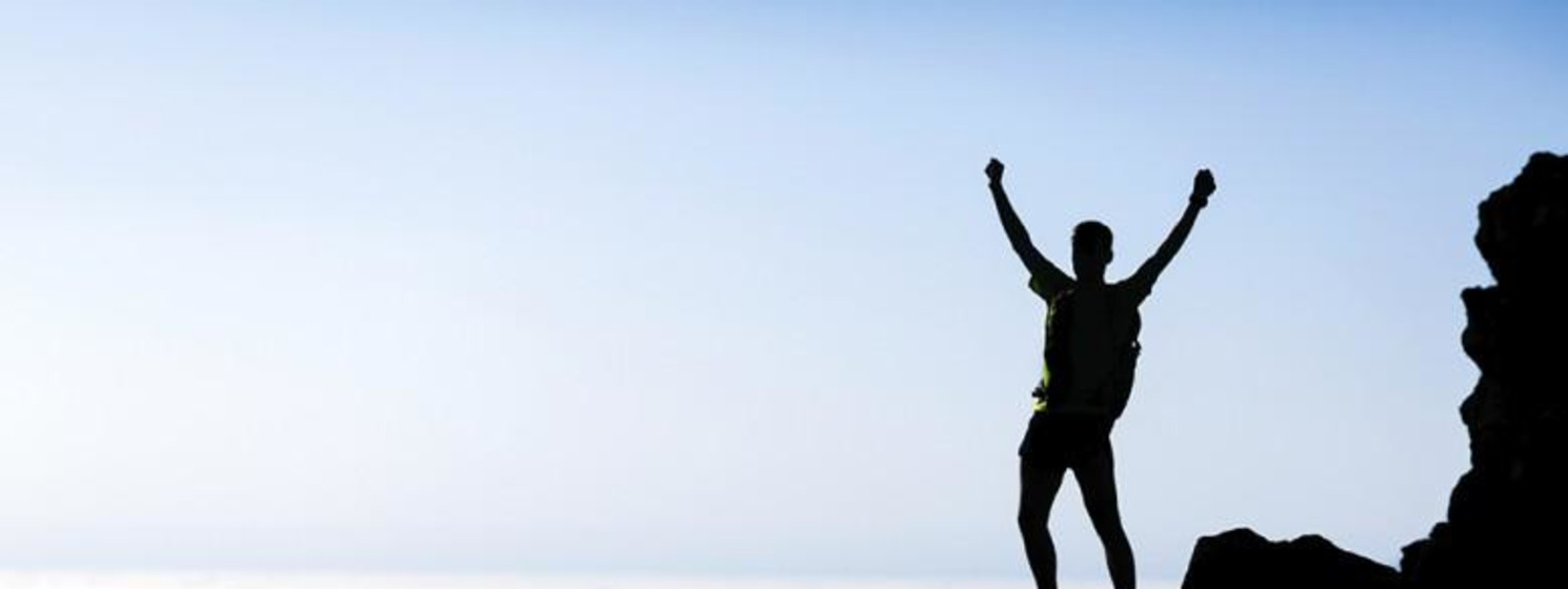 Man stands on top of mountain cliff raising hands in triumph