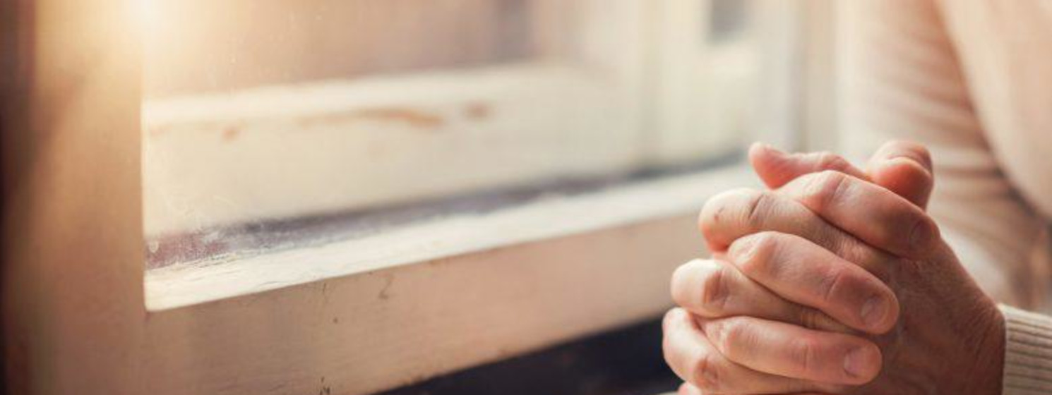 man with folded hands praying on a bible