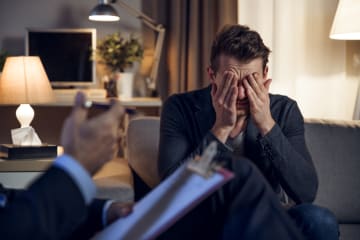 Man in suit with face in hands sitting across from woman counselor