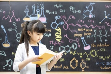 girl in lab coat using picture book for science class