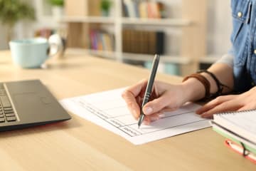 Student at a desk with laptop planning out their tasks on a paper calendar