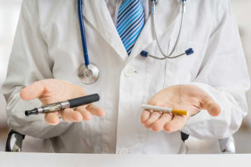 Doctor is comparing electronic vaporizer and conventional tobacco cigarette. - stock photo