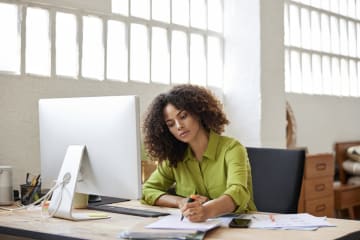 Woman writing at her desk with a notebook in an office