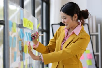 Woman brainstorms on a board with sticky notes.