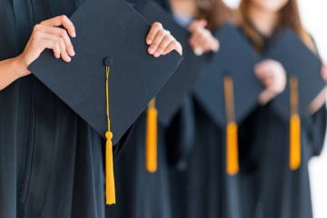 Graduating students in graduation gowns holding their caps 