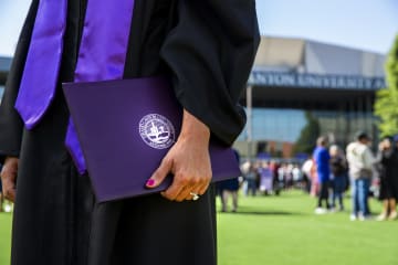 Student in cap and gown holding degree outside the Global Credit Union Arena.