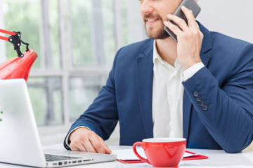 Adult man talks on cellphone sitting at a counter with a laptop 