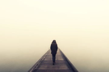 A man walking alone on a foggy bridge