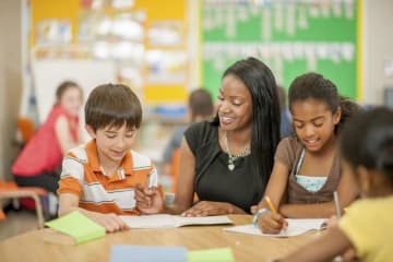 female teacher helping two young students in classroom