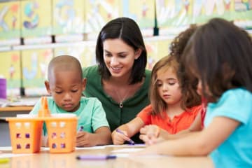 Elementary art teacher observes three kids coloring at a table