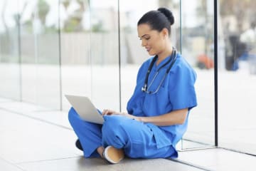 nurse sitting on floor typing on a laptop