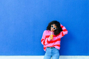 a girl sitting against a wall and drinking orange juice