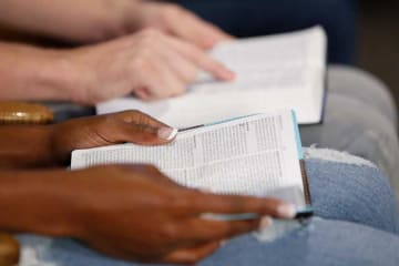 Close view of bibles opened on couples lap as they follow along