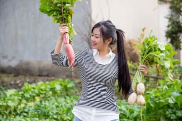 girl in a garden holding up two different vegetables