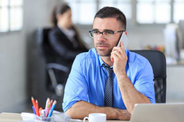 man with glasses speaking on phone in office