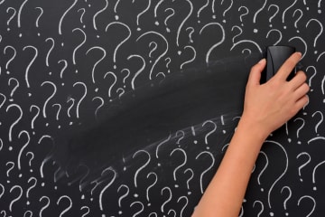 Hand erasing question marks on chalkboard
