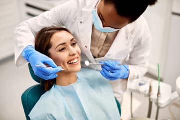 Female pre-dental student cleans female patient's teeth in office