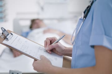 RN with nursing degree filling out paperwork beside patient