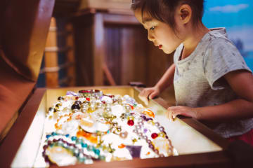 Little girl looking at pearls and other jewelry treasure in a chest