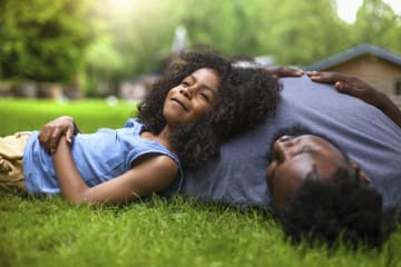 Little girl looking peaceful laying her head on her dad on the lawn