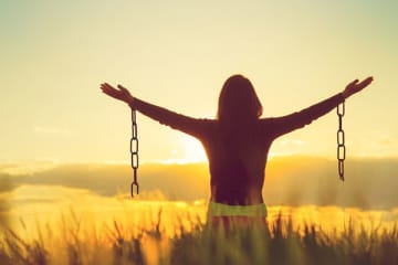 girl in field holding arms out with broken chains