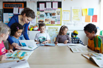 A group of elementary students reading books together with their teacher