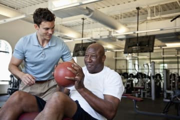 physical therapy assistant helping a patient lift a ball