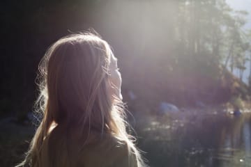 Blonde woman faces sunlight at lake shore