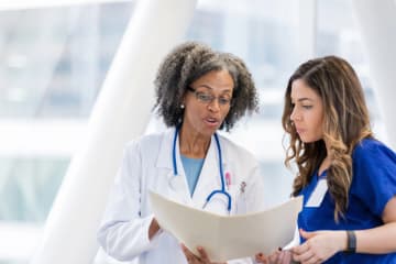 Mature female doctor discusses patient care with nurse - stock photo