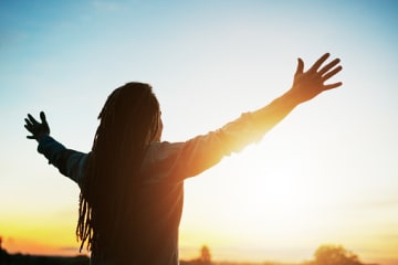 Woman admiring the sunrise with her arms raised.