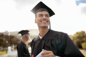 Young man outside dressed in regalia smiling and holding certificate