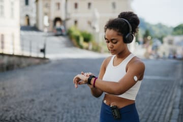 Beautiful diabetic girl in activewear checking her performance on smartwatch. Diabetic teenage girl with continuous glucose monitor and insulin pump exercising. Concept of daily life with chronic illness, diabetes for teenagers.