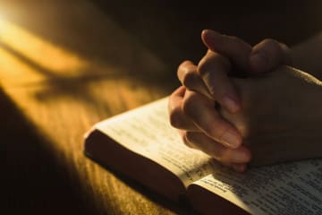 Close up of hands clasped on open Bible - stock photo