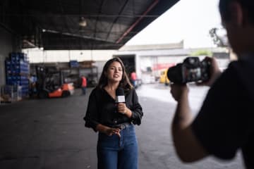 Young female broadcast journalist reporting on location