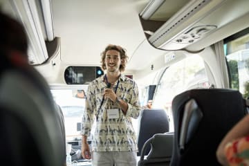 A male tour guide talking with passengers on bus