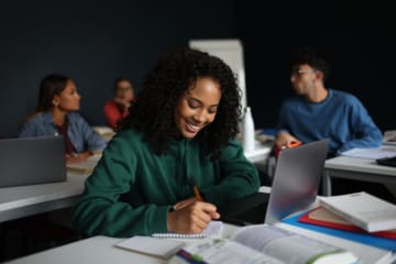 young female student smiling while writing in notebook
