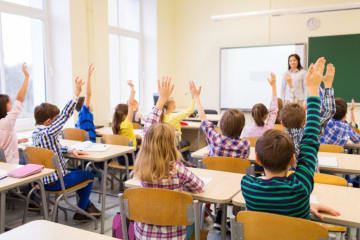 bright classroom full of students raising hands