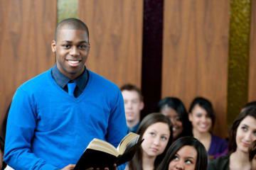 Young male pastor holds bible in full classroom