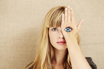 Woman covering her left eye with a painting of an eye on her hand