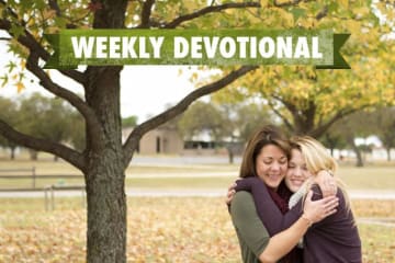 Two girls hugging under the Weekly Devotional banner