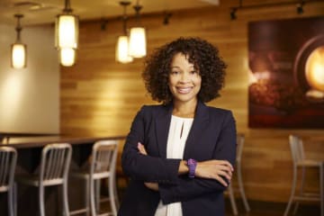 Doctoral student stands with arms crossed in a modern cafe