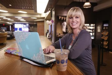 Middle-aged blonde sits a high rise table in a coffee shop