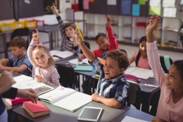 Children raise hands to answer a question in classroom setting