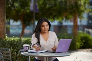 Doctoral student takes notes from laptop outdoors at GCU campus