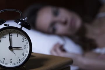 woman laying in bed looking at alarm clock