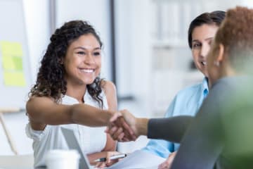 Small group of people shake hands and discuss at a table.