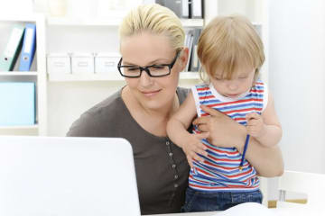 mom holding child and working on the computer