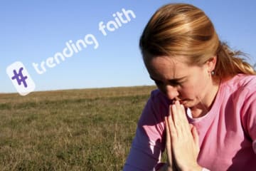 A woman praying in a field under the Trending Faith logo
