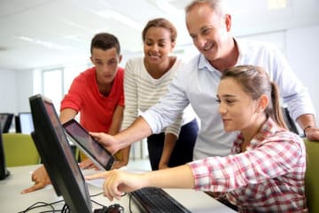 girl pointing to a computer and three other people watching