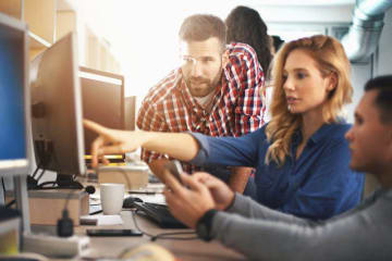 Blonde girl points at computer screen with two others helping her